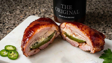 chicken thigh poppers filled with jalapenos and cream cheese on a white marble board with a bottle of The Original BBQ sauce in the back