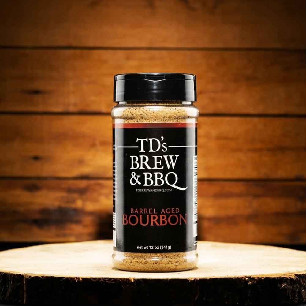 Bottle of TDs Brew & BBQ Barrel Aged Bourbon Rub on a wood plank with wood background.