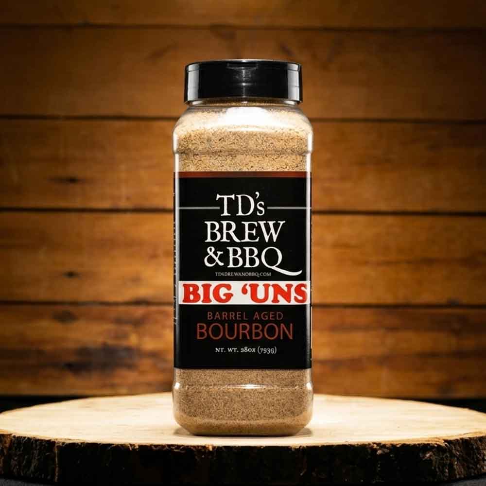 Bottle of TD's Brew & BBQ Big 'Uns Barrel Aged Bourbon seasoning on a wooden surface with a wooden background.