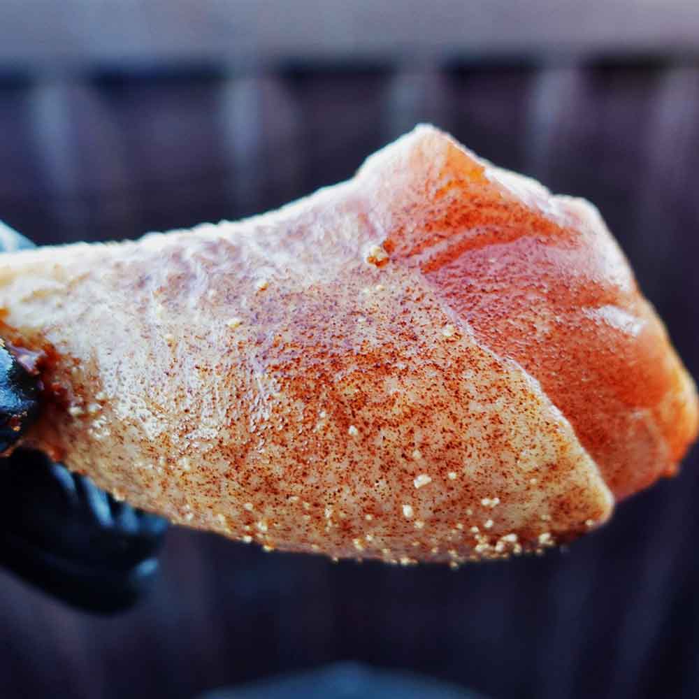 Close-up of a piece of chicken with seasoning on a grill