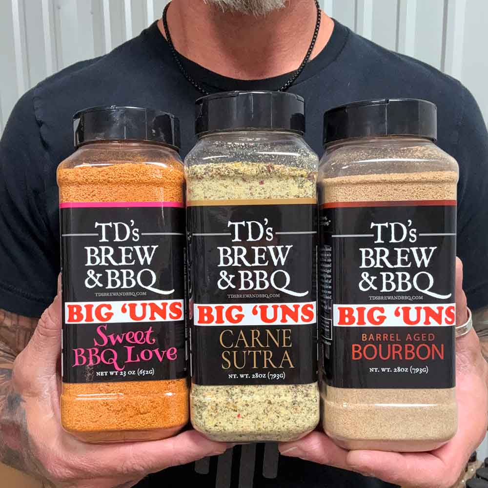 Three jars of TD's Brew & BBQ Big 'Uns seasoning on a wooden surface with a wooden background.