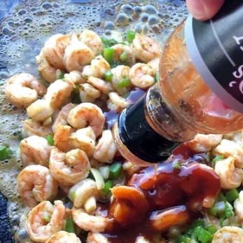 Skillet of bbq shrimp with bbq sauce being poured over