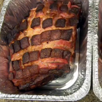 Two roasted pork shoulders with crispy bacon weave on metal trays.