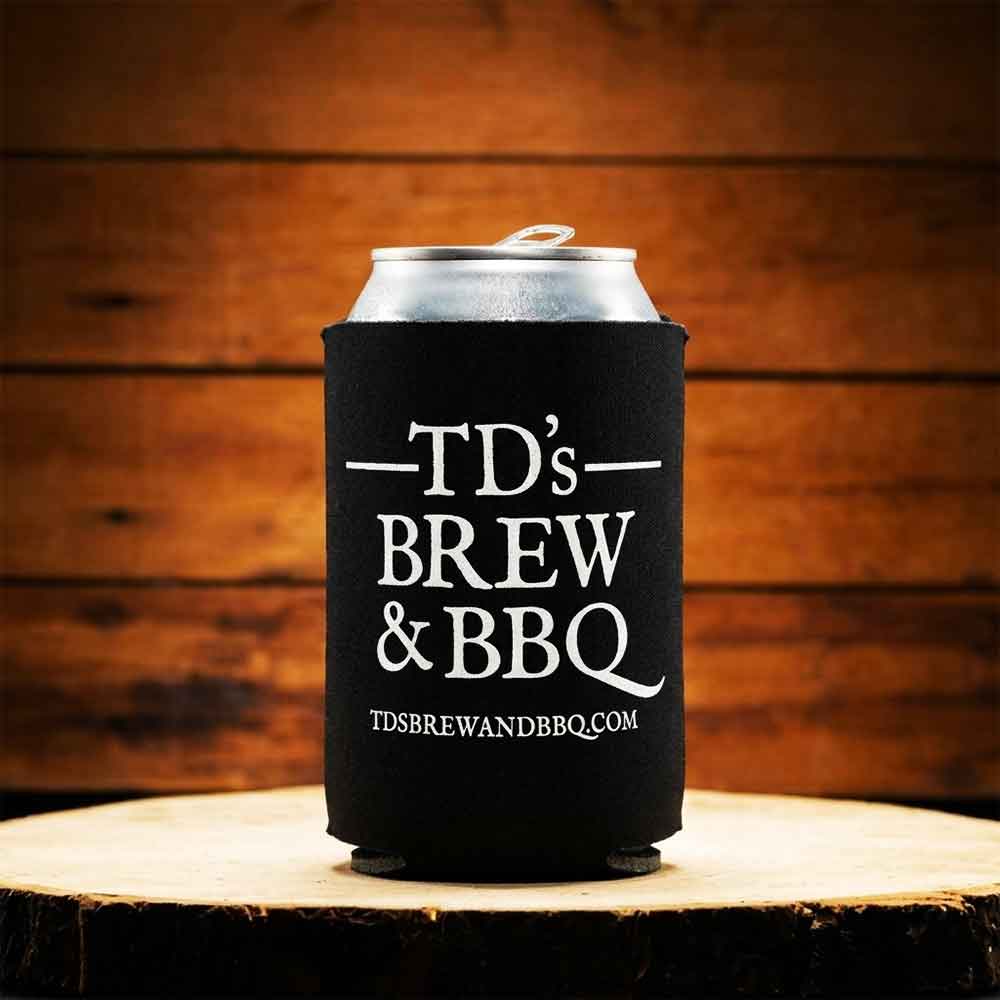 Black can cooler with 'TD's Brew & BBQ' text on a wooden surface and background