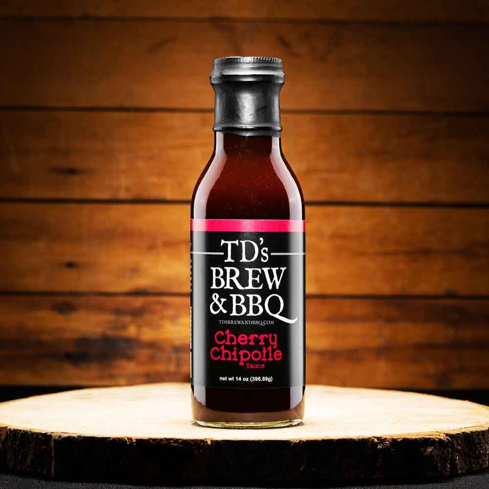 Bottle of TD's Brew & BBQ Cherry Chipotle sauce on a wooden surface with a wooden background