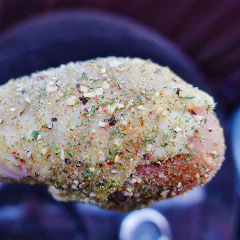 Marinaded raw chicken breast with herbs and spices on a dark background