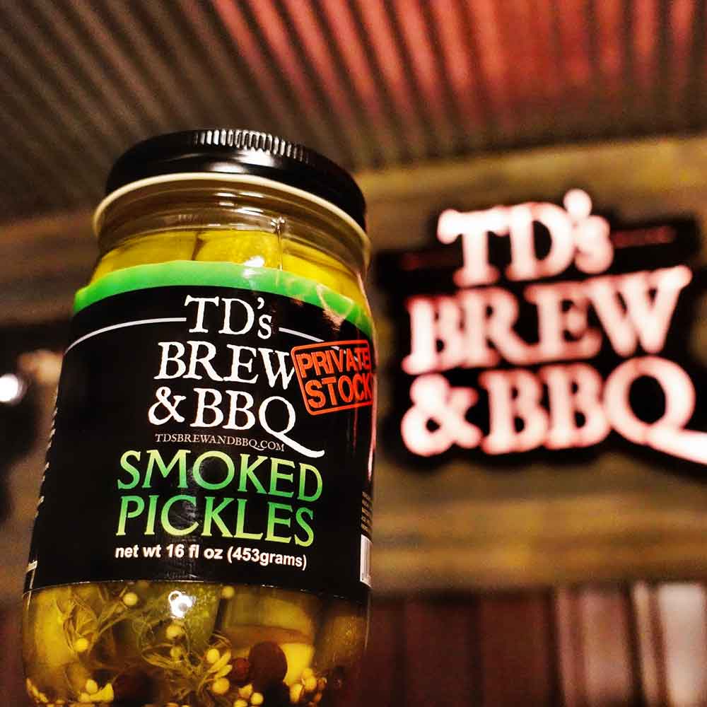 Jar of TD's Brew & BBQ Smoked Pickles on a wooden surface with a wooden background