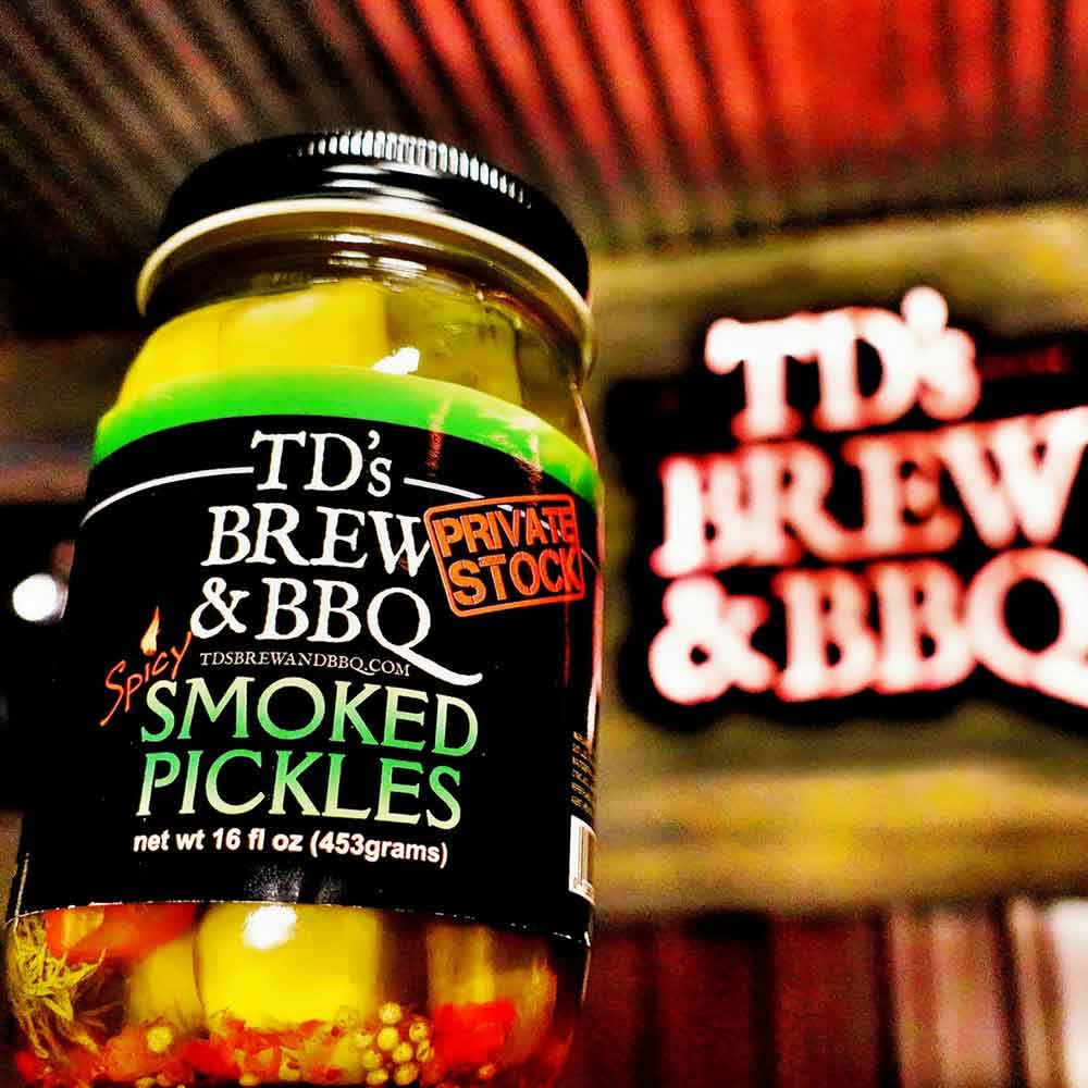Jar of TD's Brew & BBQ Spicy Smoked Pickles on a wooden surface with a wooden background