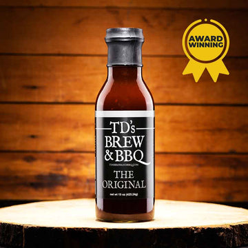 Bottle of TD's Brew & BBQ sauce on a wooden surface with an award badge in the corner.
