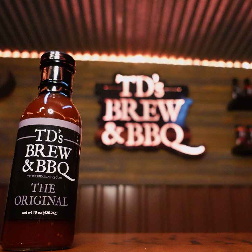 Bottle of TD's Brew & BBQ sauce with a neon sign in the background