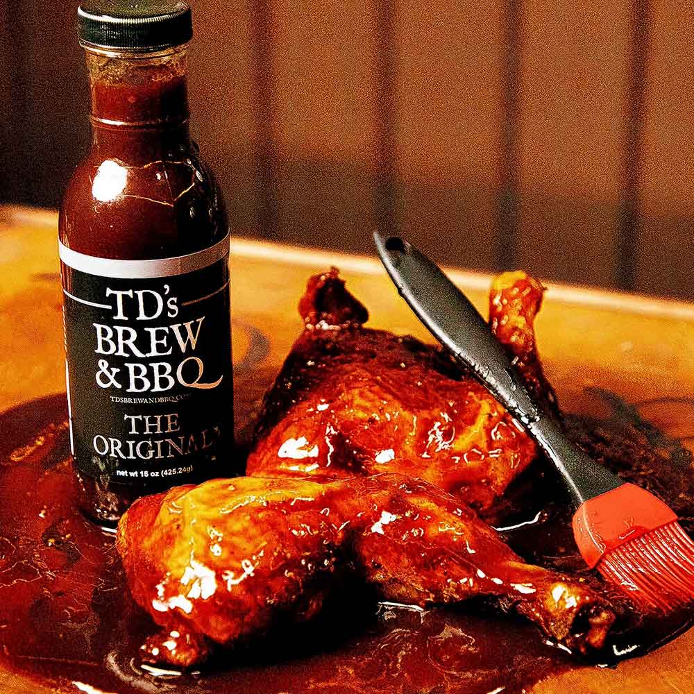 Bottle of TD's Brew & BBQ sauce with roasted chicken on a wooden surface