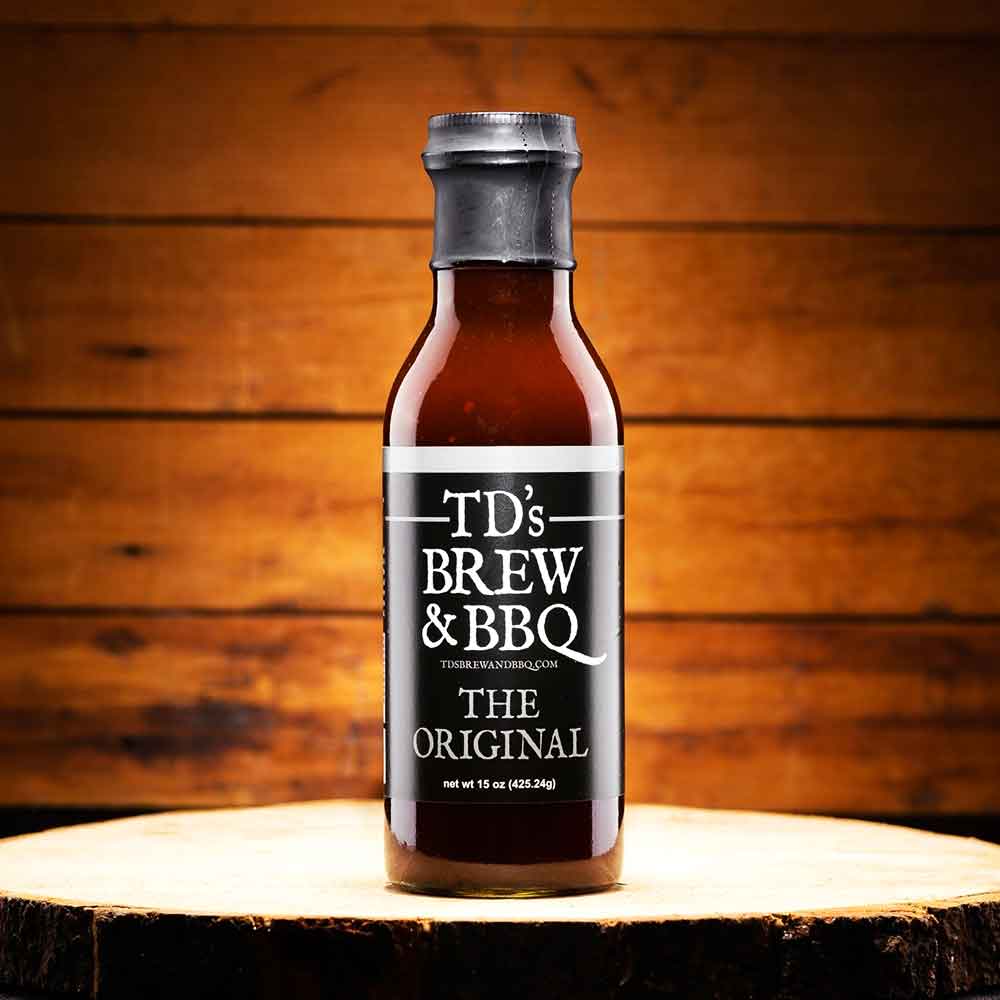 Bottle of TD's Brew & BBQ sauce on a wooden surface with a wooden background
