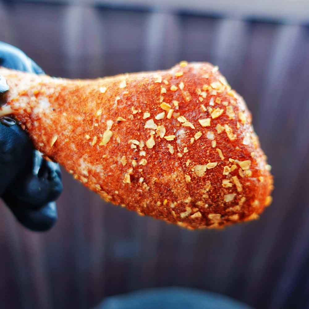 Seasoned chicken drumstick held by a gloved hand against a blurred background