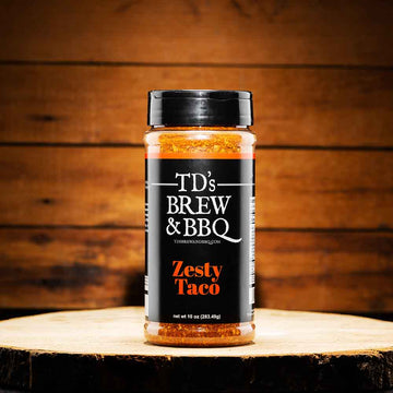 Jar of TD's Brew & BBQ Zesty Taco seasoning on a wooden surface with a wooden background
